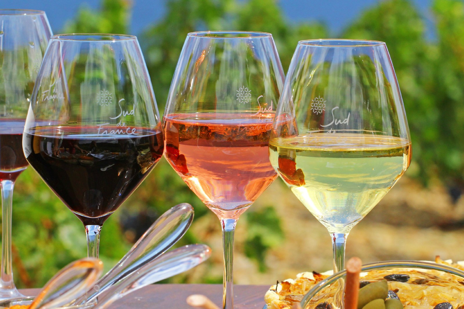 three glasses with Sud de France logo etched on them, one with red wine, one with white wine, one with rosé